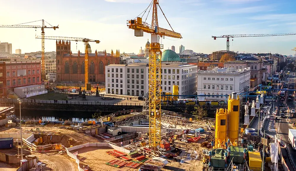 Urban construction site with multiple yellow tower cranes and heavy machinery operating amidst historic and modern buildings